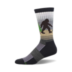 Crew socks in dark gray, beige, and white, featuring a Bigfoot walking through a forest.  Green trees and a subtle striped pattern.