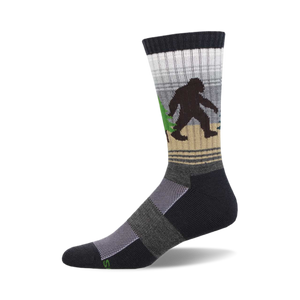 Crew socks in dark gray, beige, and white, featuring a Bigfoot walking through a forest.  Green trees and a subtle striped pattern.