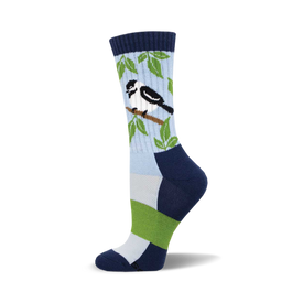 the blue sock has a pattern of green leaves and small black and white birds with a yellow or gold beak. the top of the sock is navy blue with a lighter blue toe and heel.