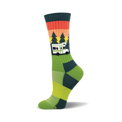 the green sock has a pattern of orange, red, and brown stripes near the top. below that are green pine trees of different heights. there is a white camper van with black windows and the word "home" on the front in black text. the bottom of the sock is yellow with two thin green stripes above the yellow.