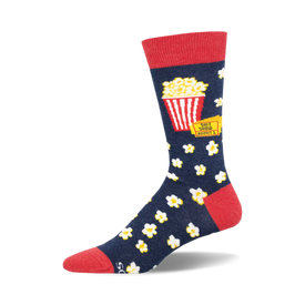 socks that are blue with a red top. there is a picture of a red and white striped popcorn bucket on the socks with the words 'shit show' above it and 'admit 1' below it. there are also white popcorn kernels all over the socks.