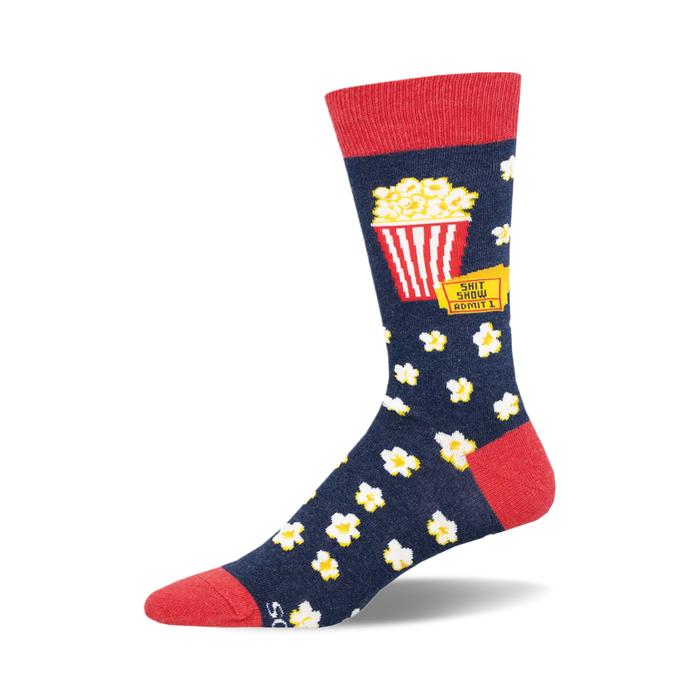 socks that are blue with a red top. there is a picture of a red and white striped popcorn bucket on the socks with the words 'shit show' above it and 'admit 1' below it. there are also white popcorn kernels all over the socks. }}