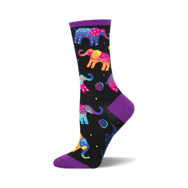 socks that are black with a pattern of multicolored elephants. the elephants have pink, blue, yellow, green, and orange colors. there are also some small white stars and yellow and white flowers in the background. the top of the sock is purple.