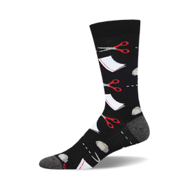 socks that are black and have a pattern of red scissors and grey rocks scattered all over. there is also a white square with a dotted line around it to represent paper.