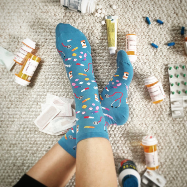 Close-up of 'Meds' socks in blue; the design showcases pills, syringes, and stethoscopes. [lf]