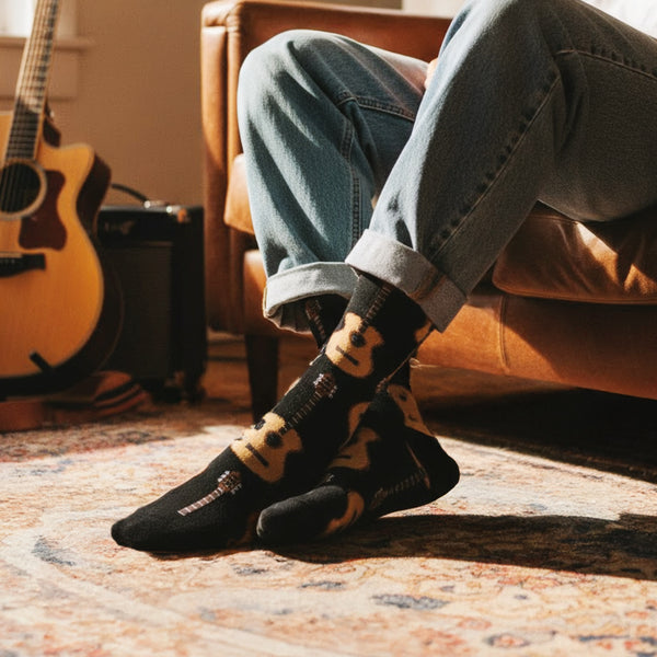 Person in cuffed jeans wearing black crew sock with golden acoustic guitar pattern, lounging indoors. [lf]