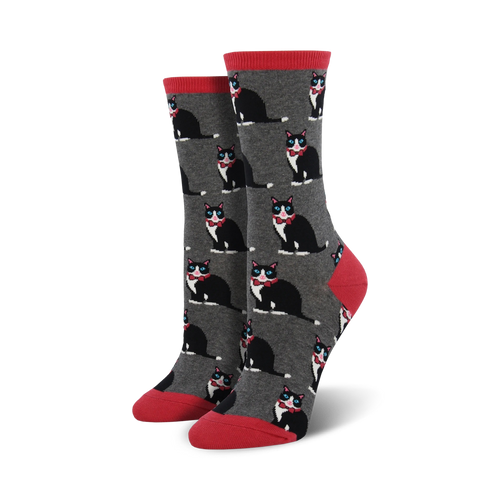 A pair of women's crew socks in gray with a repeating pattern of black tuxedo cats wearing red bow ties. The socks have coral red cuffs.