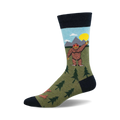 Crew socks in olive green, navy blue, and light blue, featuring a cartoon Bigfoot waving, mountains, and little trees.