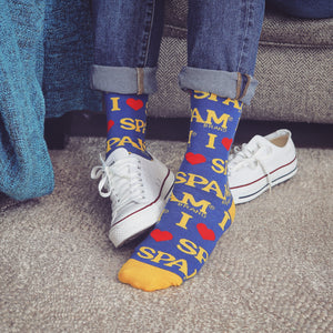 A person is wearing blue jeans, white sneakers, and socks with a yellow background and red heart design that says 