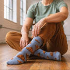 Person in green tee & brown pants wearing light blue croissant pattern crew socks, sitting on a wooden floor. [lf]