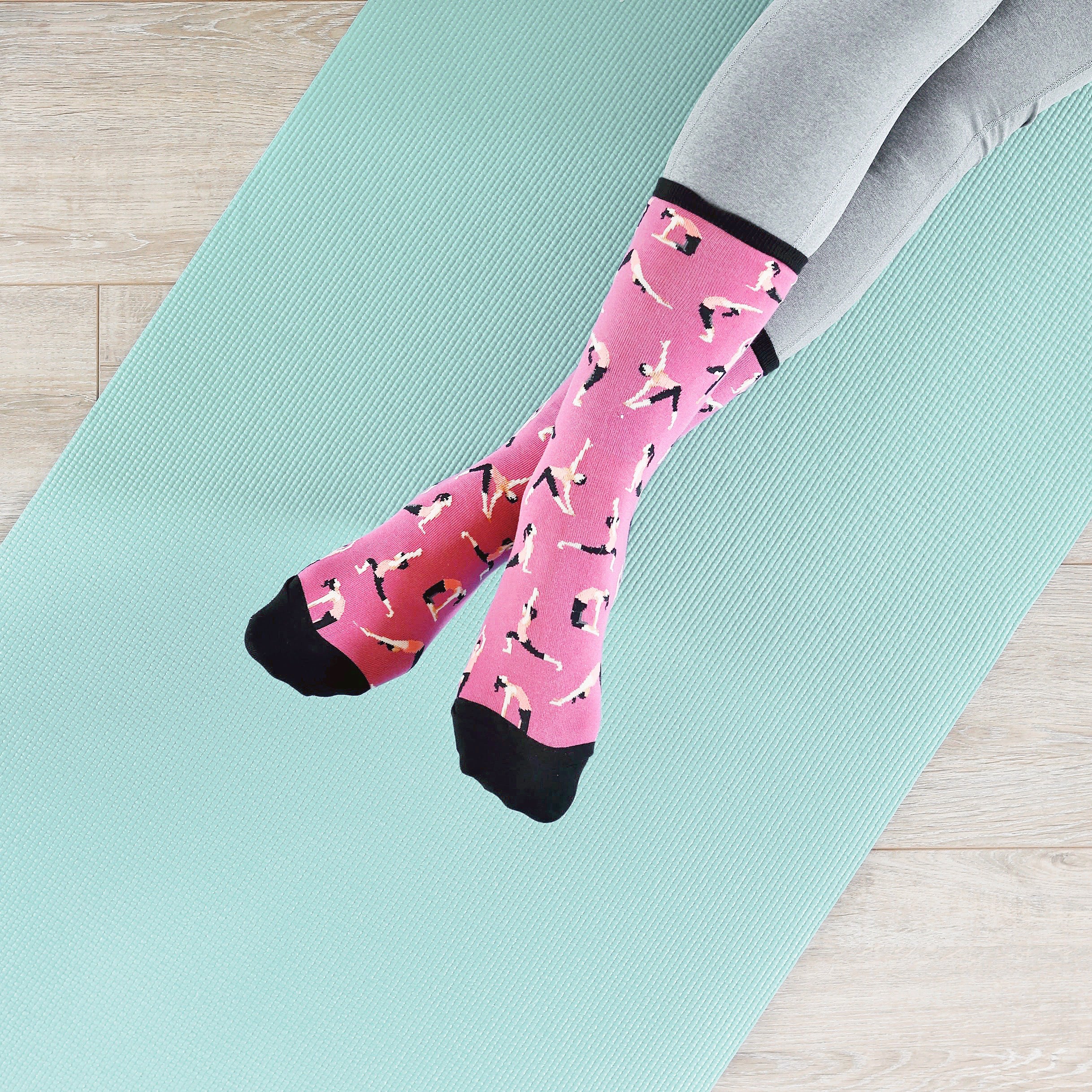 Lifestyle shot showing a person's legs wearing pink yoga socks on a teal yoga mat. [lf]