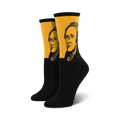 Pair of black and gold crew socks featuring a portrait of Alexander Hamilton. The socks have a mustard yellow band with a black and white illustration of Hamilton's face.