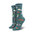 A pair of women's crew socks in teal with a whimsical pattern of orange carrots, tomatoes, teapots, and kitchen utensils.