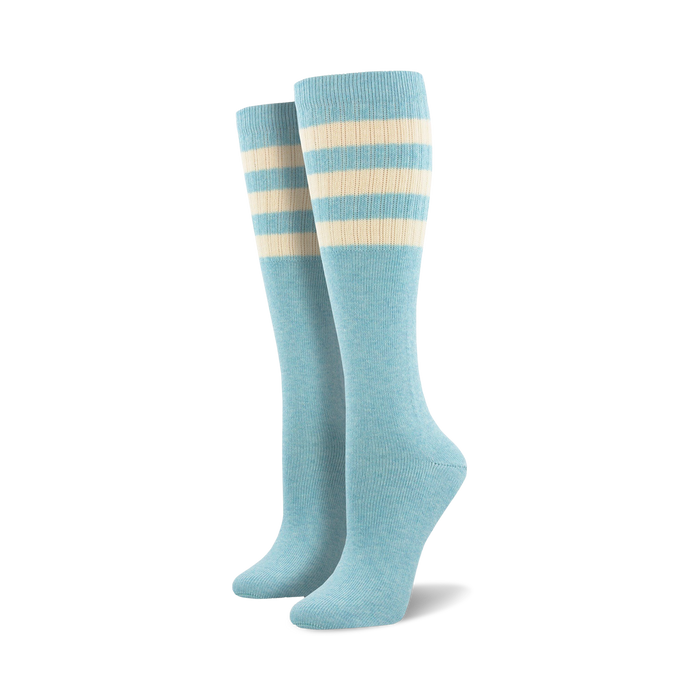 Pair of light blue knee-high socks with a vibrant rainbow striped cuff against a white background.