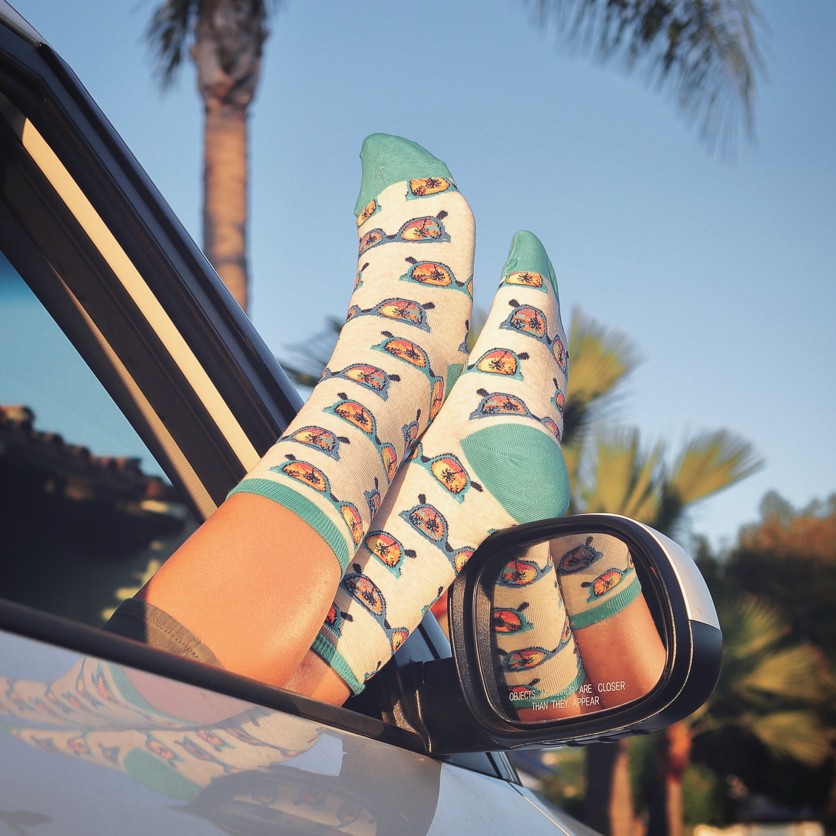 Lifestyle shot of a woman's feet in Seeshore socks hanging out of a car window. [lf]