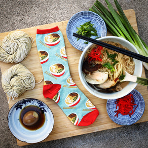 A person is wearing a pair of red leather sandals and blue socks with a ramen pattern.