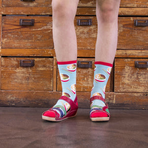 A person is wearing a pair of red leather sandals and blue socks with a ramen pattern.