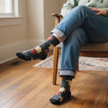 Model wearing dark grey crew socks with red chili & yellow corn patterns, cuffed jeans, seated indoors. [lf]