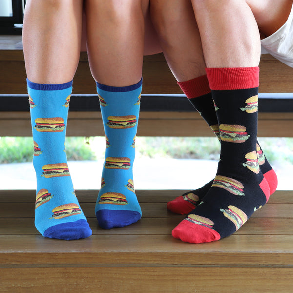 Lifestyle shot: Two people sitting on a bench, showing off their Good Burger socks; one pair is light blue, the other is black. [lf]