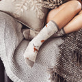 Lifestyle shot of a person relaxing with their legs up, wearing the cream-colored Winter Forest socks. [lf]