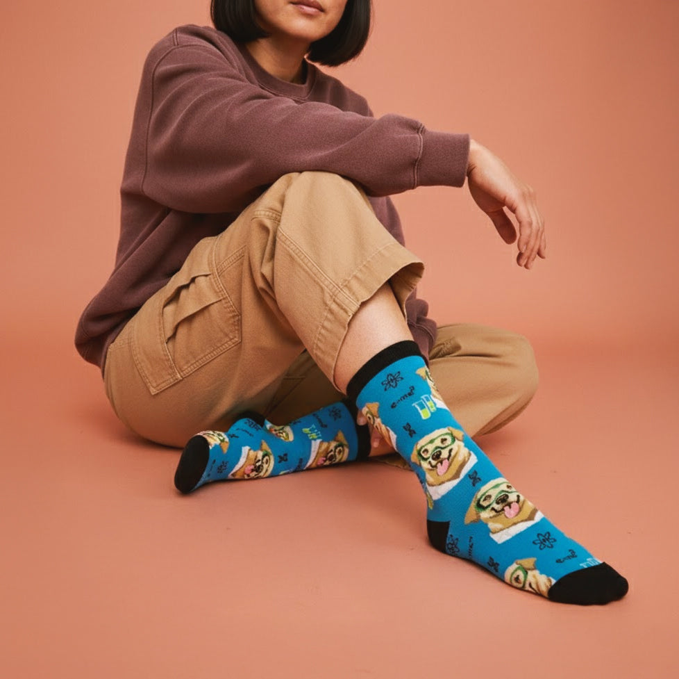 Person sitting, showing blue crew socks with a science dog in green goggles pattern, paired with tan pants. [lf]