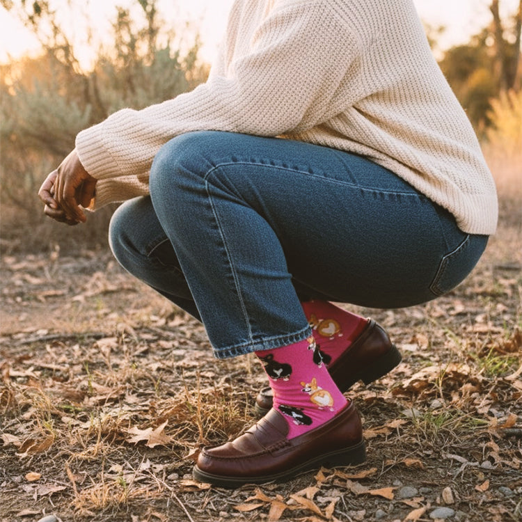 Model crouching in jeans & loafers, showcasing bright pink Corgi pattern crew sock outdoors. [lf]