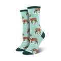 Lifestyle shot of a person's feet wearing teal Winter Reindeer socks. The background shows snow and nature.