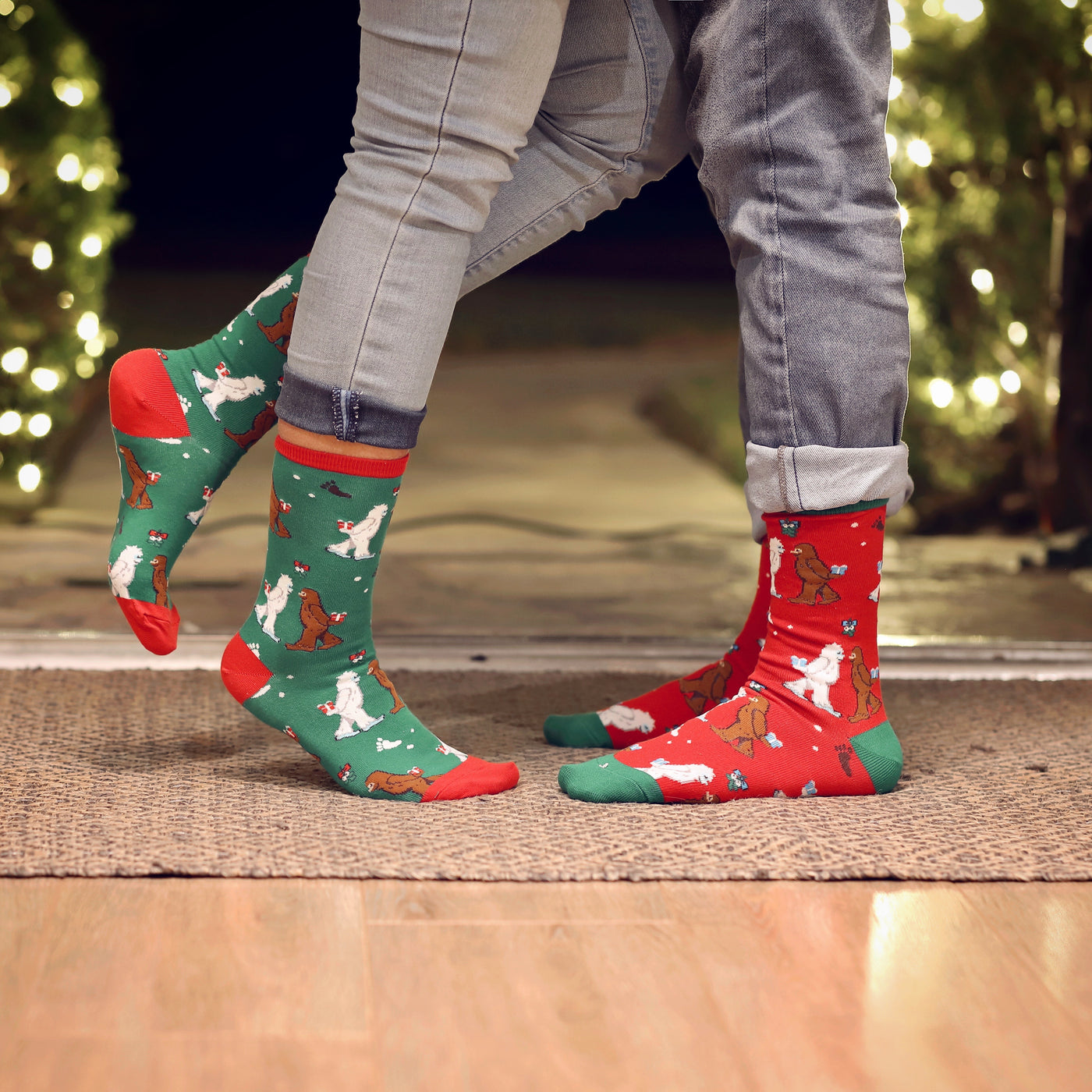 Lifestyle shot of a couple wearing Mythical Kissmas socks in red and green.  Christmas lights are in the background. [lf]