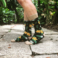 Lifestyle shot of Aloha Floral socks on a person's legs outdoors, showcasing the socks against a garden backdrop. [lf]