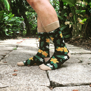 A person is standing on a stone path in a garden. They are wearing black socks with a floral pattern of white and yellow flowers and brown and white striped cuffs.