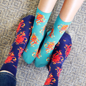 A pair of blue socks with a red octopus pattern and a pair of green socks with an orange octopus pattern.