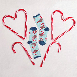 A pair of blue socks with a pattern of sloths wearing Santa hats. The socks are surrounded by four candy canes in the shape of hearts.