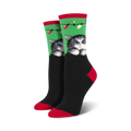Pair of women's crew socks. Black background, green and red accents, cute gray cat peeking over the top with holiday lights.