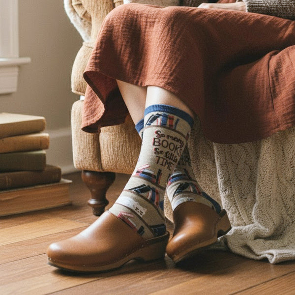 Model wearing brown clogs & a rust dress, showing a tan crew sock with book pattern and 'So many books, so little time' text. [lf]