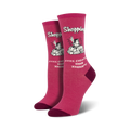 Pair of women's crew socks in pink featuring a retro-style illustration of a woman shopping with the text 'Shopping Still Cheaper Than Therapy'.