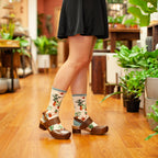 Lifestyle shot of a woman in a black skirt wearing Home Grown socks and brown clogs in a plant shop. [lf]