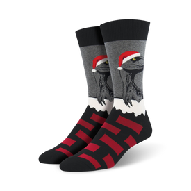 black and gray crew socks with a repeating pattern of red and black squares and a cartoon dinosaur wearing a santa hat standing on snow.   