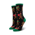 A pair of women's crew socks with a black background. Bigfoot characters wear Santa hats and carry Christmas trees. Green cuffs and red accents.