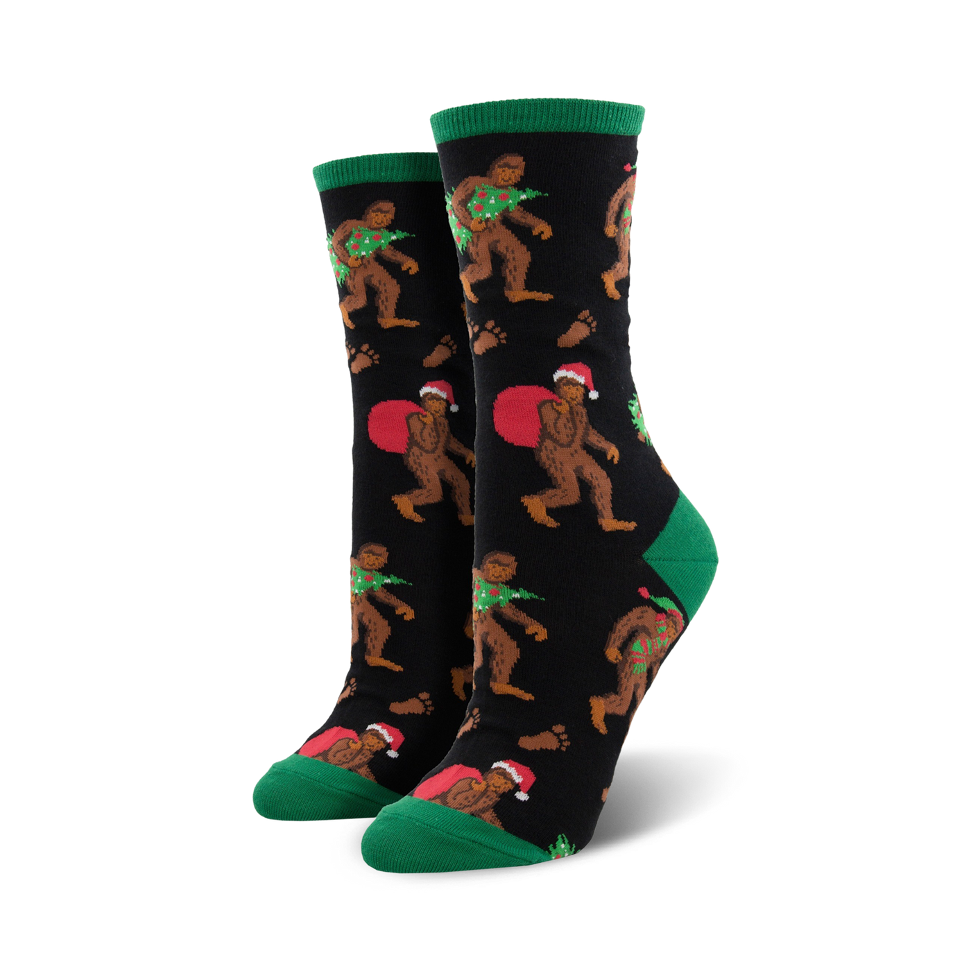 A pair of women's crew socks with a black background. Bigfoot characters wear Santa hats and carry Christmas trees. Green cuffs and red accents.