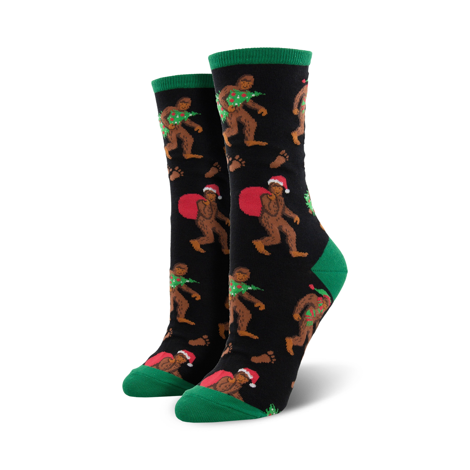 A pair of women's crew socks with a black background. Bigfoot characters wear Santa hats and carry Christmas trees. Green cuffs and red accents.