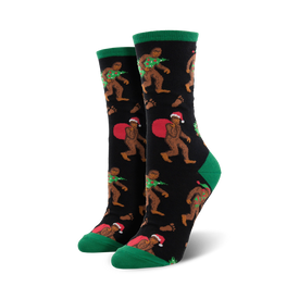 womens black crew socks with cartoonish brown bigfoot in red santa hats, carrying a christmas tree or sack of presents. green toes and cuffs.  