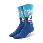 Pair of blue crew socks with a sailboat design on a water scene.  Light blue sky, green shoreline, and a red and white sailboat are featured on a navy blue background.