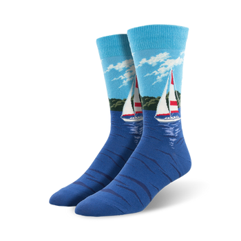 Pair of blue crew socks with a sailboat design on a water scene.  Light blue sky, green shoreline, and a red and white sailboat are featured on a navy blue background.