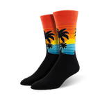 Pair of crew socks with a sunset, palm trees, and ocean wave design.  The socks are mainly black with orange, yellow, and teal accents.