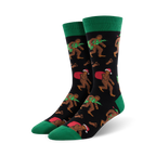 Pair of crew socks; black background with Bigfoot carrying a Christmas tree and Santa sack; green cuffs; red and green accents.