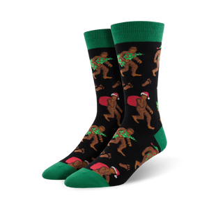 Pair of crew socks; black background with Bigfoot carrying a Christmas tree and Santa sack; green cuffs; red and green accents.
