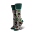 A pair of grey crew socks with brown Bigfoot and green trees. The socks have teal cuffs.
