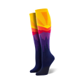 Pair of women's knee-high socks showcasing a vibrant sunset over silhouetted mountains. Colors include yellow, orange, red, purple, and navy blue.