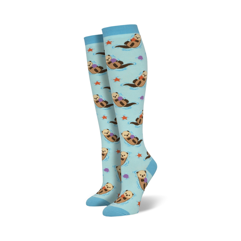 Pair of light blue knee-high socks featuring a repeating pattern of otters holding rocks, alongside starfish and seashells.