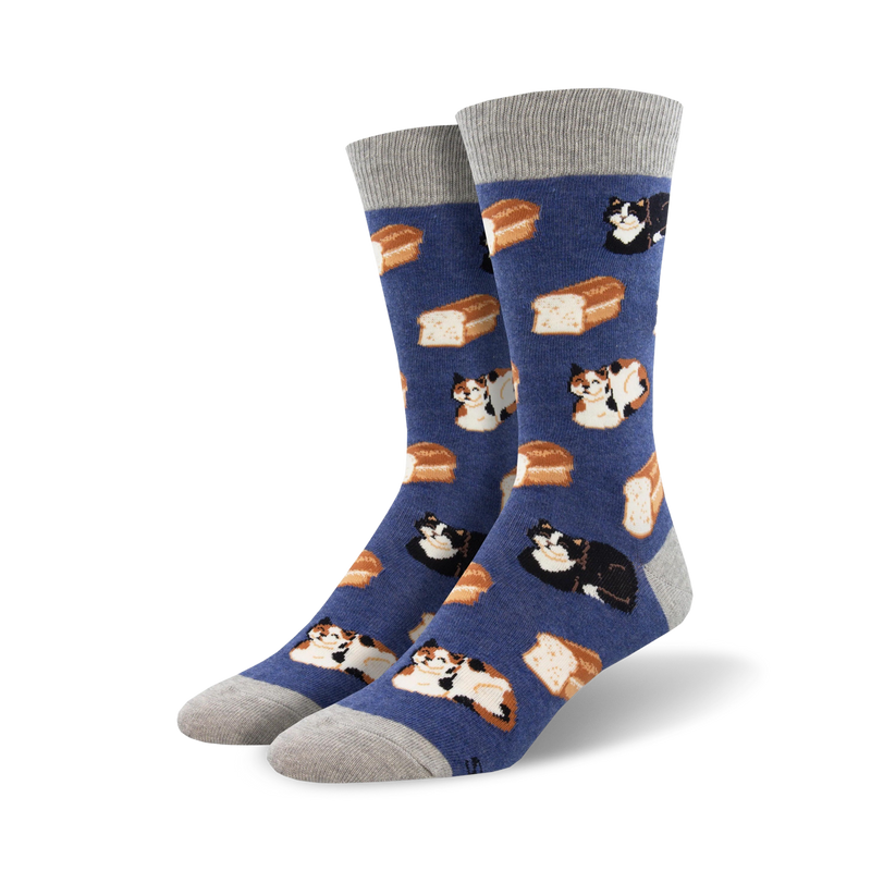 A pair of crew socks in blue with a pattern of cats and bread loaves. The cats are calico and black. The socks have gray cuffs.